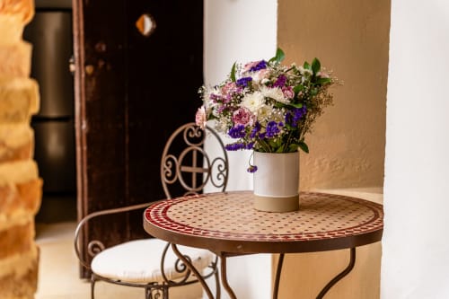 Arreglo floral colorido en jarrón blanco sobre mesa redonda decorativa con silla de hierro forjado en la villa Casa de Medina, Medina