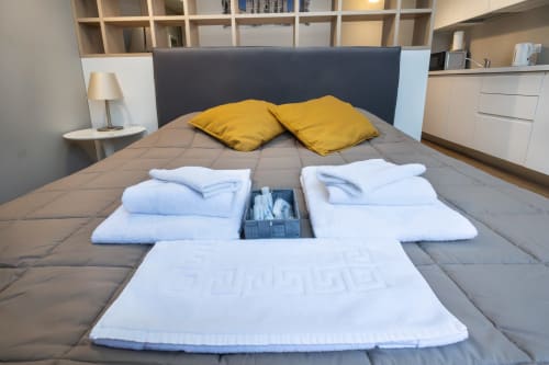 Schlafzimmer der Magnolia Apartments Mailand mit gelben Kissen, grauer Bettwäsche, weißen Handtüchern und moderner Einrichtung mit Stadtblick