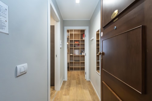 Moderner Flur in den Magnolia Apartments Mailand mit Holzboden, eingebauten Regalen, dunkelbraunen Türen und weißen Wänden
