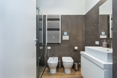 Modernes Badezimmer in den Magnolia Apartments Mailand mit weißem Waschbecken, Toilette, Bidet, beheiztem Handtuchhalter und Holzfußboden
