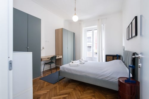 Habitación moderna en Magnolia Apartments Milan con cama, escritorio, armario, puertas de balcón, parquet y vistas a la ciudad