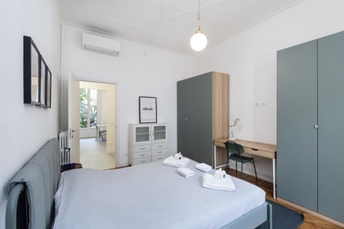 Dormitorio moderno en Magnolia Apartments Milan con cama, armario, escritorio y vista al jardín por la puerta abierta
