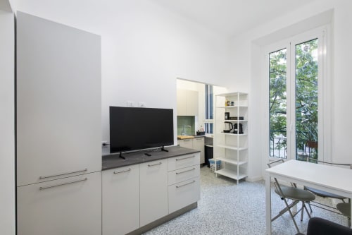 Cocina y sala de estar modernas de planta abierta con gabinetes blancos, televisor de pantalla plana, mesa de comedor y vista al jardín