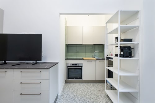 Cocina moderna y sala de estar en apartamento milanés con electrodomésticos empotrados, salpicadero de azulejos verdes y estanterías blancas