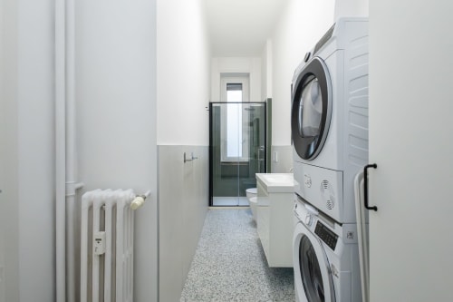 Lavandería moderna en Magnolia Apartments Milan con lavadora-secadora apiladas, paredes blancas y diseño minimalista
