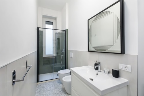 Baño moderno en Magnolia Apartments Milan con vanidad blanca, mampara de ducha verde oscuro, espejo y piso de baldosas grises