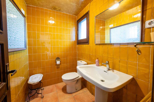 Baño con azulejos amarillo brillante, lavabo blanco, inodoro y espejos en Masia Rural Ca l'Eloi Janet cerca de Barcelona