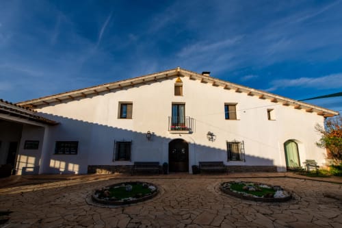 Masía Rural Ca l'Eloi Janet: casa de labranza tradicional encalada con vigas de madera, patio y cielo azul, Barcelona