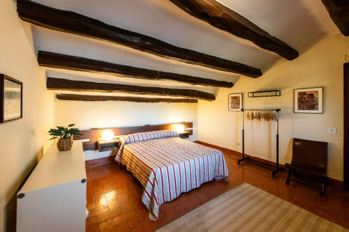 Dormitorio rústico en Masía Rural Ca l'Eloi Janet, Barcelona, con vigas de madera vistas, suelos de barro y ropa de cama a rayas