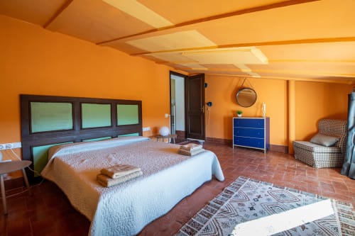 Amplio dormitorio con paredes naranjas, techo de vigas de madera, cómoda azul y suelo de terracota en Masia Rural Ca l'Eloi Janet
