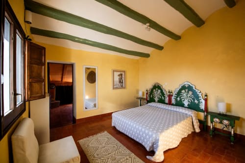 Dormitorio amarillo brillante con vigas de techo verdes en Masia Rural Ca l'Eloi Janet cerca de Barcelona, con cabecero ornamentado