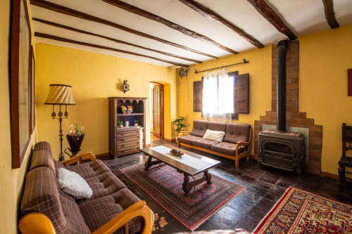 Acogedor salón amarillo con vigas de madera, chimenea y mobiliario tradicional en Masia Rural Ca l'Eloi Janet, Barcelona