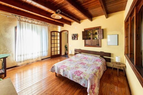 Espacioso dormitorio en Masia Rural Ca l'Eloi Janet con vigas de madera, paredes amarillas y ropa de cama floral con vistas a Barcelona