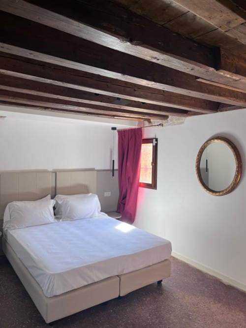 Camera da letto accogliente con letto matrimoniale al Casanova Hideaway Venice, travi in legno a vista, specchio rotondo e tende rosa alle finestre