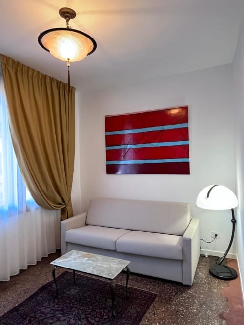 Camera Deluxe Doppia Casanova Hideaway a Venezia con divano grigio, opere d'arte a righe rosse, tende dorate e lampada a soffitto