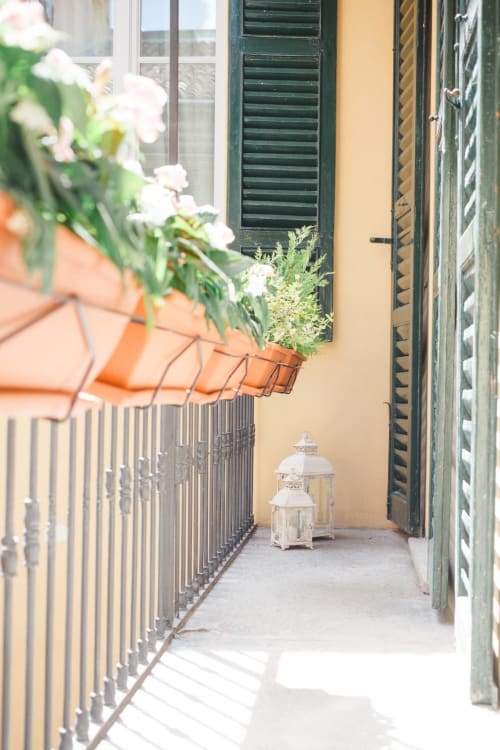 Charming narrow balcony at Alessia's Place Como with white flowers, green shutters, decorative lanterns, and terracotta