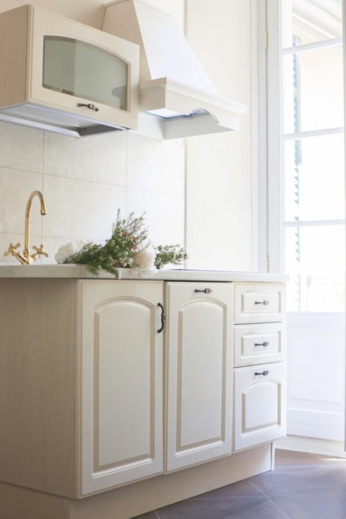 Modern kitchen in Alessia's Place Como suite with cream cabinetry, brass faucet, white subway tile backsplash, and natural