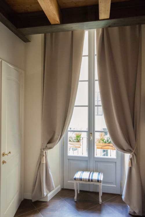 Elegant suite at Alessia's Place in Como with tall windows, beige curtains, wooden beams, and a striped bench overlooking the