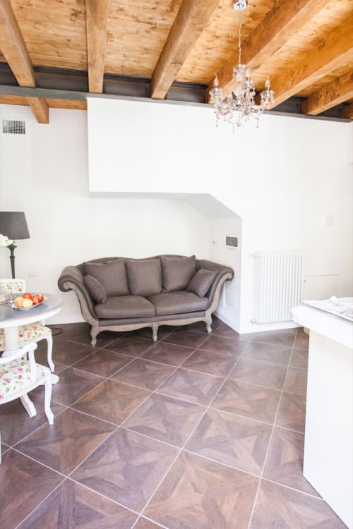 Elegant living area in Alessia's Place Como apartment with gray sofa, exposed wooden beams, crystal chandelier, and patterned