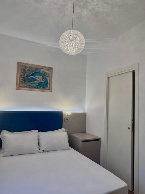 Cozy double bedroom at Casanova Hideaway Venice with blue headboard, white bedding, and modern pendant light
