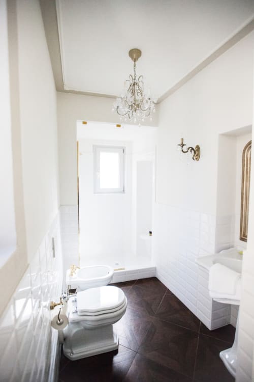 Modern bathroom in Alessia's Place Como suite with marble floors, white subway tiles, rainfall shower, and crystal chandelier