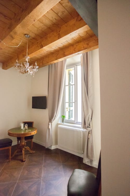 Suite 3 ad Alessia's Place Como: elegante zona living con travi in legno a vista, lampadario in cristallo, tavolo rotondo, ampio