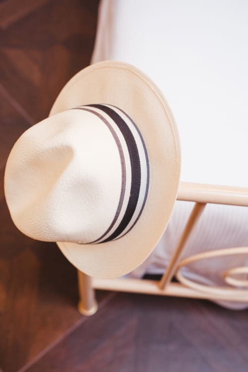 Cream-colored straw hat with dark band displayed on wooden rack at Alessia's Place Como