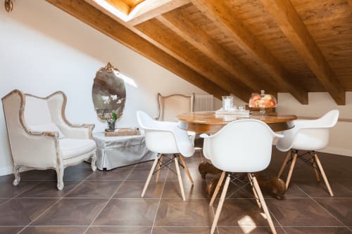 Modern dining area in Alessia's Place Como suite with round wood table, white chairs, exposed wooden beams, and city views.