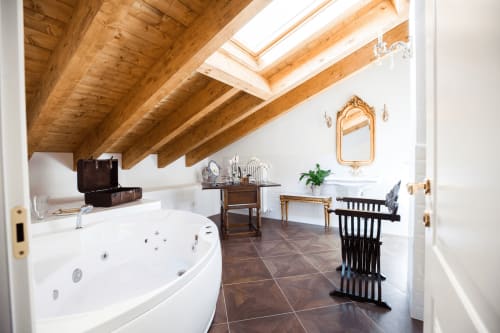 Luxurious bathroom in Alessia's Place Como with Jacuzzi tub, exposed wood beams, skylight, and elegant furnishings.