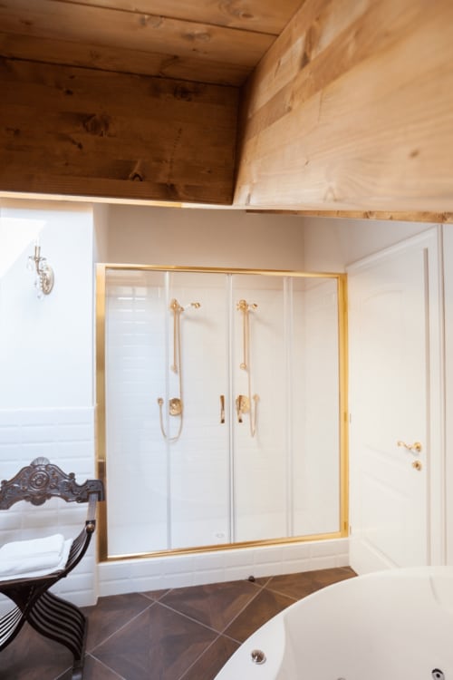 Luxury bathroom in Alessia's Place Como suite with gold-framed glass shower enclosure, white tile walls, and dark tile