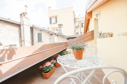 Sunny terrace at Alessia's Place Como with white furniture, potted flowers, and city views of historic buildings