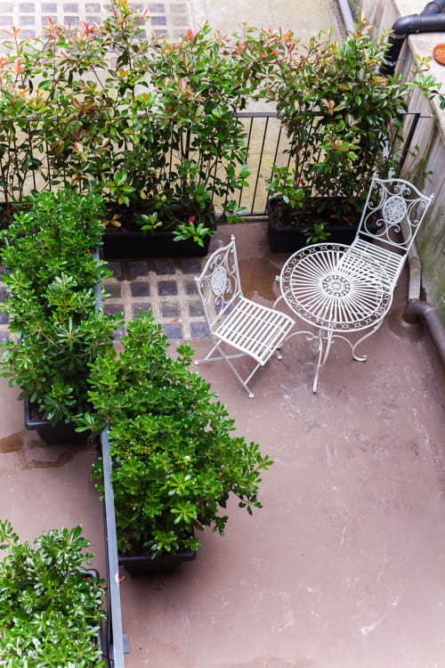 Cozy terrace at Alessia's Place Como with ornate white chairs, potted plants with red flowers, and brick patio.