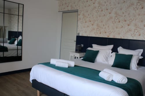 Elegant double bedroom at Domaine des Piéris with garden view, black headboard, green accents, rolled towels, and floral