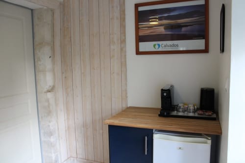 Kitchenette corner in Domaine des Piéris room with wooden counter, coffee machine, refrigerator, and framed coastal artwork