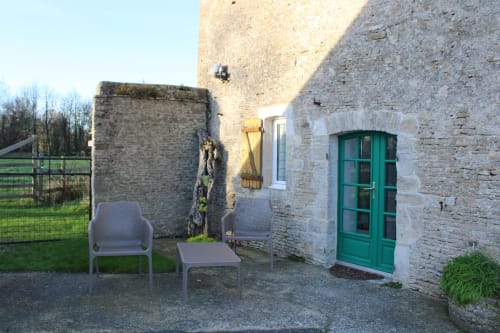 Stone cottage exterior at Domaine des Piéris with green door, seating area, and garden view in Grandcamp-Maisy