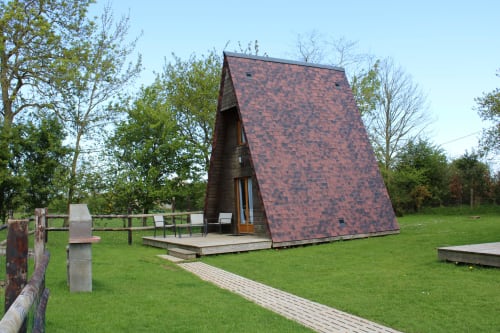 Modern wooden lodge cottage at Domaine des Piéris with red-tiled A-frame roof in garden setting, Grandcamp-Maisy
