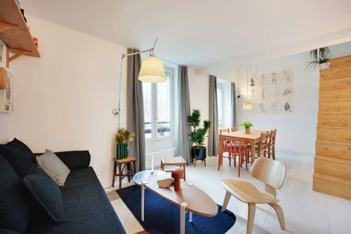Salon contemporain parisien avec canapé noir, coin repas, mobilier bois et grandes fenêtres à la Conciergerie Saint
