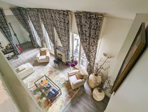 Chambre élégante à la Conciergerie Saint Martin Paris avec rideaux à motifs, fauteuils crème et éléments décoratifs