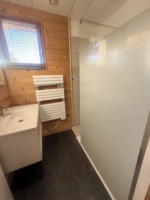 Salle de bain moderne du gîte Des Planchettes avec lavabo blanc, porte-serviettes chauffant, douche à l'italienne et murs en bois