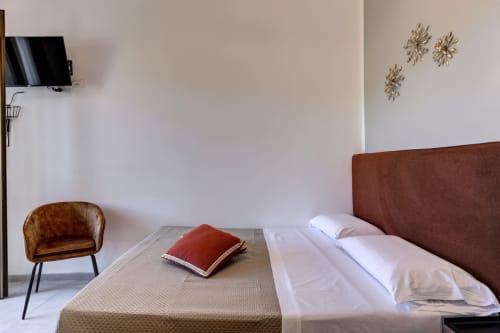 Modern hotel room at Palazzo Belvedere with brown upholstered bed, terracotta chair, and wall décor in Chianciano Terme