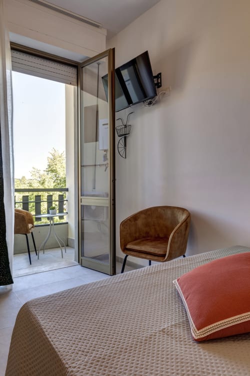 Modern hotel room at Palazzo Belvedere with brown leather chair, bed, wall-mounted TV, and balcony overlooking Chianciano