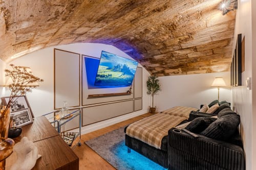 Luxurious Bordeaux apartment suite with exposed stone ceiling, flat-screen TV, black bed with checkered bedding, and modern