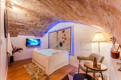 Luxury spa suite in Bordeaux with arched brick ceiling, jacuzzi, TV, and modern seating area