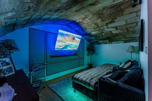 Modern cinema suite in Bordeaux with vaulted stone ceiling, blue lighting, bed, flat-screen TV displaying landscape, and spa