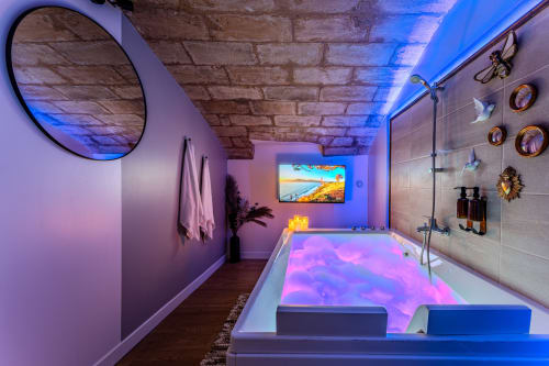 Luxury spa bathroom at Wellkhome Bordeaux with illuminated jacuzzi, arched brick ceiling, mood lighting, and wall-mounted TV