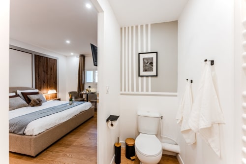 Wellkhome Bordeaux suite bathroom with toilet and towel rack, adjoining bedroom with bed and TV