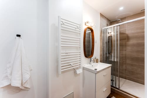 Modern bathroom in Bordeaux apartment with white vanity, walk-in shower, heated towel rack and wooden mirror