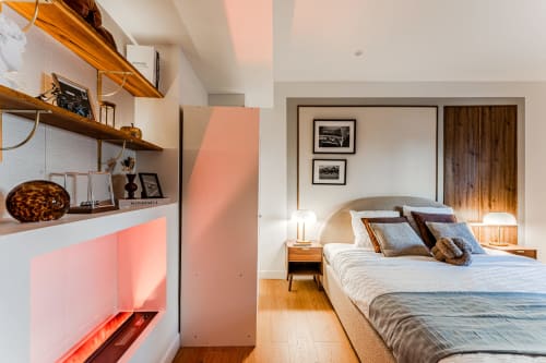 Modern Bordeaux apartment suite with wooden shelving, bed with pillows, nightstands, hardwood floors, and ambient lighting