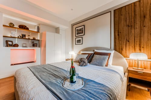 Wellkhome luxury apartment bedroom in Bordeaux with wooden wardrobe, modern bed, champagne bottle, and city views