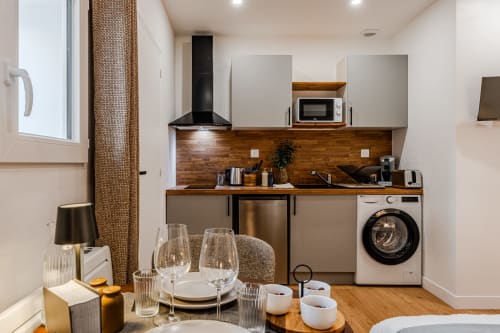 Modern kitchen-dining area in Bordeaux apartment with wood backsplash, stainless steel appliances, and place settings